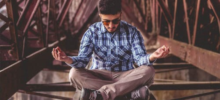 A man in a checkered shirt meditating on a metal surface, showing self-efficacy in addiction recovery.