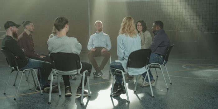 People sitting in a circle during group therapy to deal with self-harm and addiction.