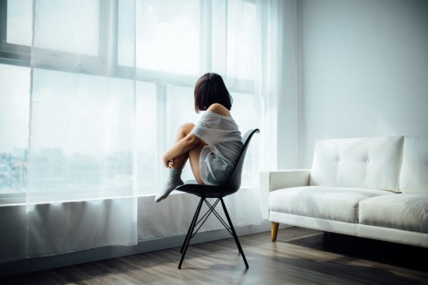 Woman sitting alone on a chair in a white room.