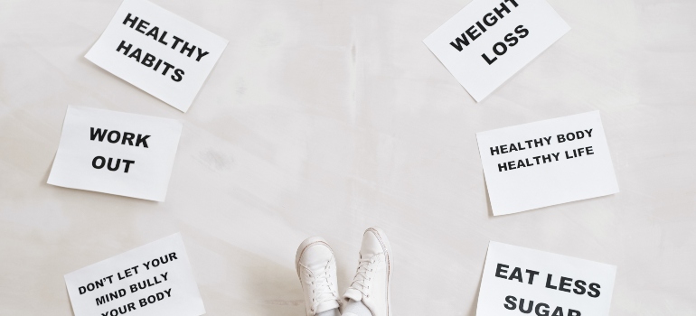 various healthy habits printed on paper and lain on the floor around a person's feet