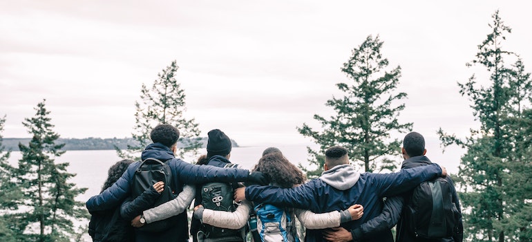 a group of friends hiking in the woods and higging each other while looking at a view and talking about the history of addiction treatment and drug rehab