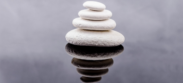Stacked white rocks reflecting on water, symbolizing alternative therapies for addiction through a holistic approach to recovery.
