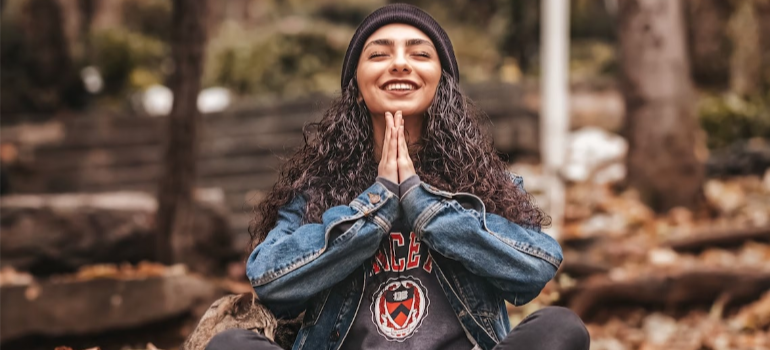 A smiling young woman meditating outdoors.