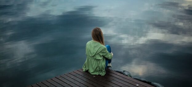 Person sitting alone by a body of water.