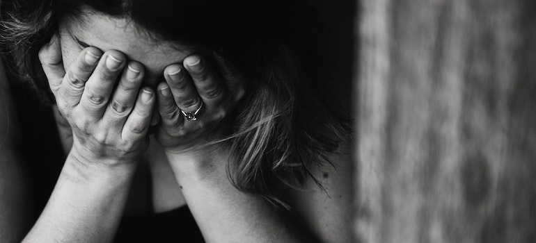 A black and white photo of a woman with her hands covering her face, suffering from stress