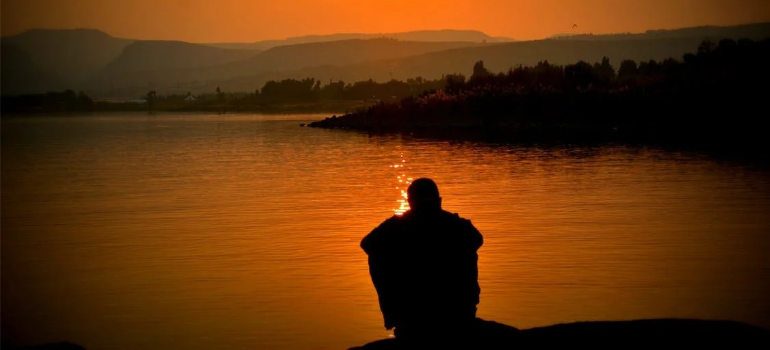 An unrecognizable person sitting by a body of water.