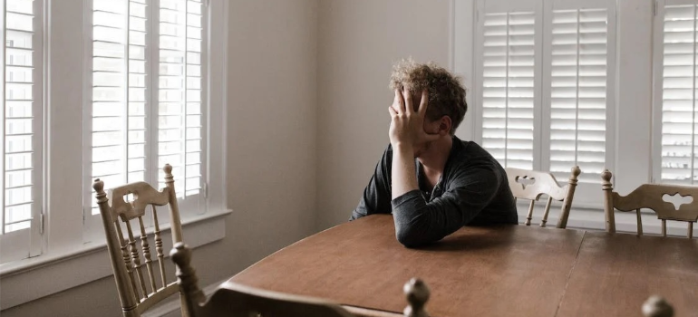 A close-up of a depressed man leaning on a wooden table.
