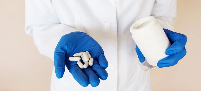 A close-up of a medical professional presenting pills out of a bottle.