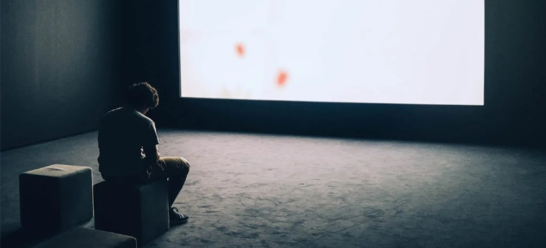 A depressed man in front of a large screen, illustrating the need for early intervention in addiction treatment.