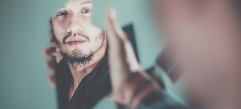 A man looking into his reflection on a piece of glass.