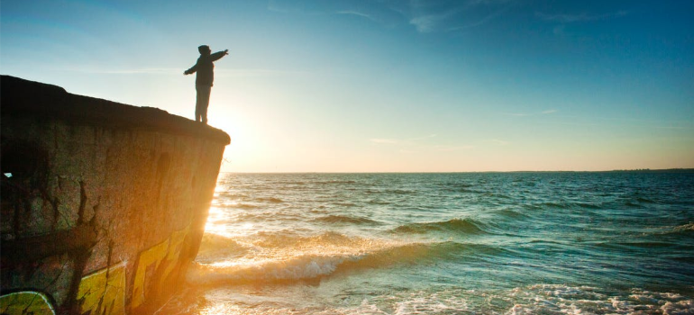 The silhouette of a person by a body of water under sunlight.