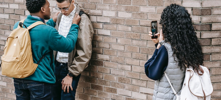 A boy bullying another bot by pushing him against a wall and a girl filming it