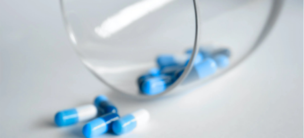 A glass containing white and blue medicine pills.