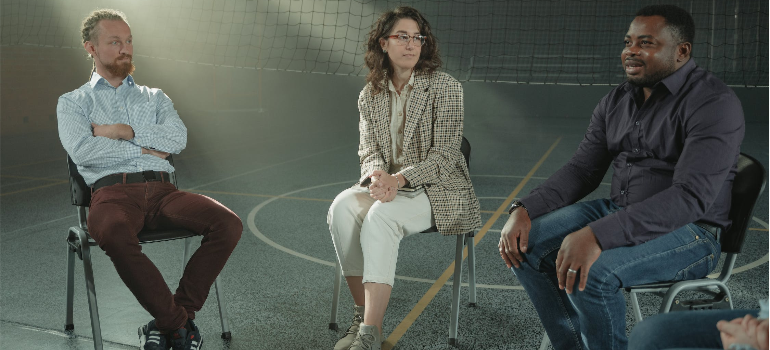 Two men and a woman during a group therapy session indoors, illustrating how psychotherapy helps with long-term effects of benzodiazepine addiction.
