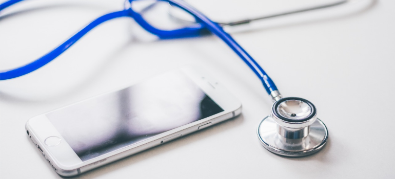A close-up of a mobile phone next to a stethoscope.