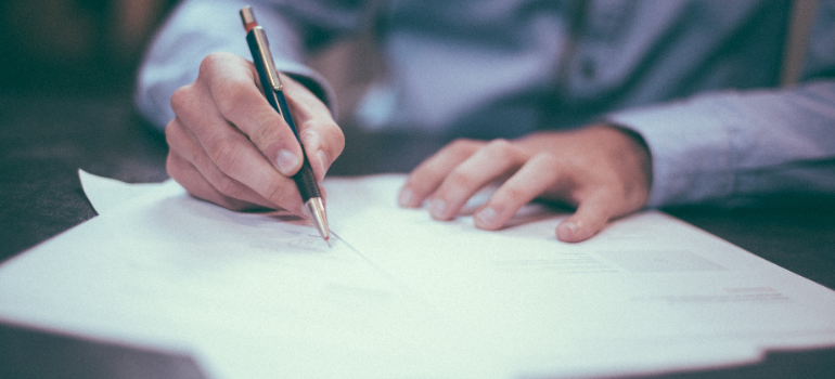 A man is writing something on a few pieces of paper on the table.