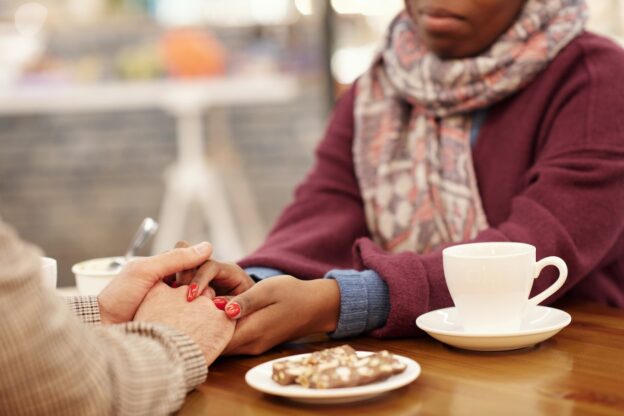 Two women holding hands in a café representing the social type of substance abuse recovery capital
