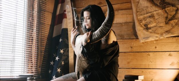 a woman smoking weed and sitting with a bull skull thinks about the Impact of Addiction on the Local Native American Population in West Virginia