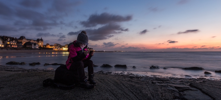 A woman using her phone at the beach representing technology-induced escape from reality