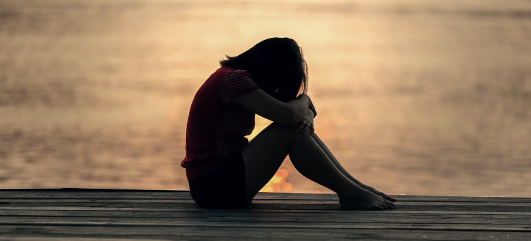 A girl sitting near a body of water during sunset