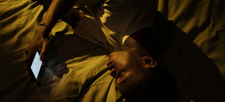 A person with post-acute withdrawal syndrome (PAWS) lying in bed and looking at his phone