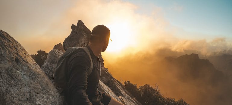 man rock climbing and looking at the sun.