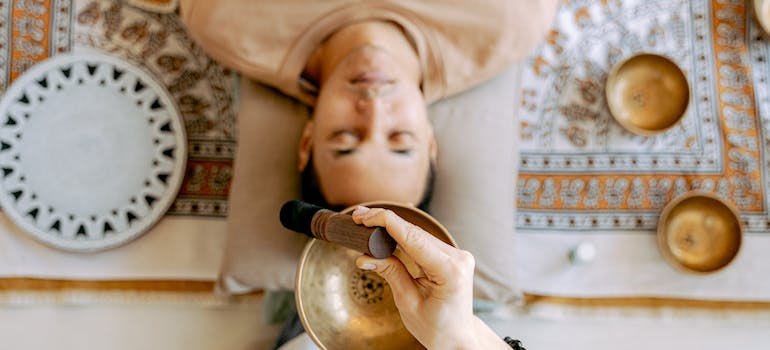 A person lying on the floor while another person uses an instrument above his head during sound bat therapy