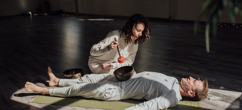 A man laying on the floor while a woman performs sound bath therapy