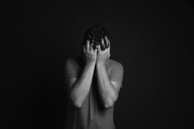A black and white photo of a person covering their face with their hands, representing the link between marijuana and schizophrenia