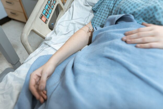 Person sitting in a hospital bed after discussing does alcohol cause cancer with a doctor.