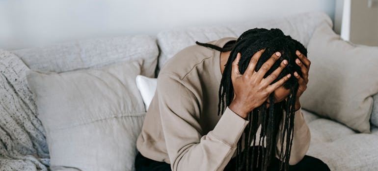 Man sitting on the couch and holding his head.