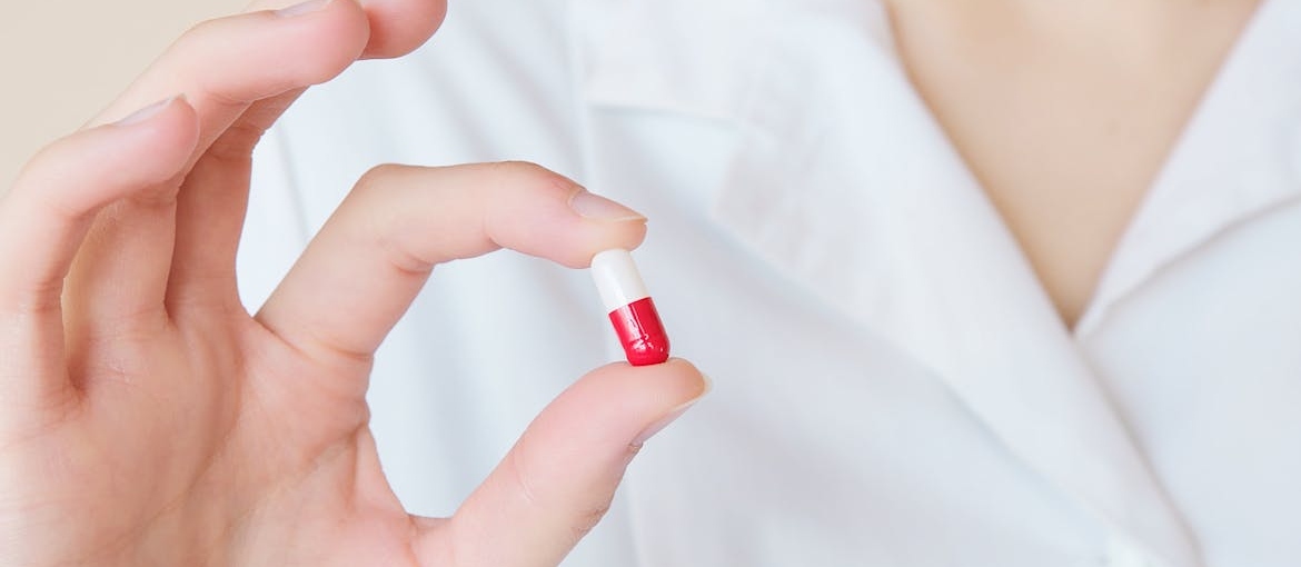 Person holding a red and white pill.