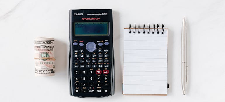 Notepad and a calculator next to a wad of cash.