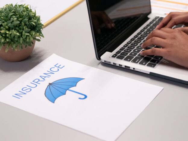 Person researching how to prevent surprise rehab bills with insurance papers next to the laptop.