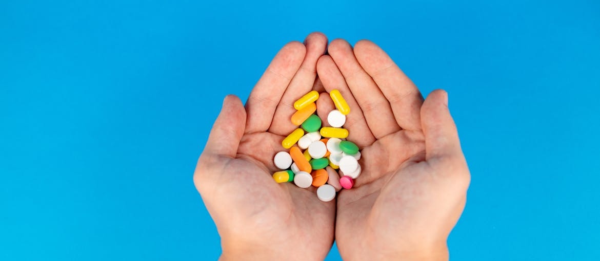 A person holding colorful pills that are drugs associated with violent acts.