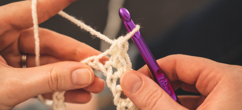 Two hands crocheting with white yarn