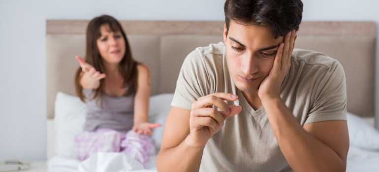 A couple argues on a bed, the woman is blurred and seems to be making an argument while a man looks at a pill