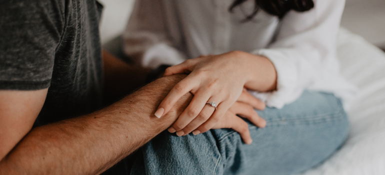 A couple holds hands but we only see their laps