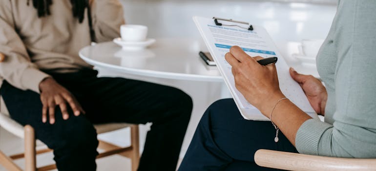 Woman taking notes on a clipboard while talking to a man.