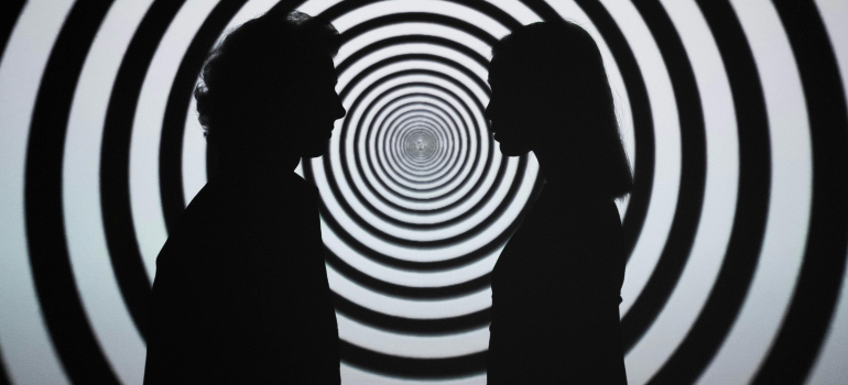 Silhouette of 2 people standing in front of white and black stripe wall symbolizing hallucinations