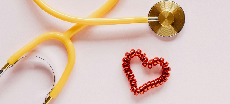 stethoscope near decorative coil tie in heart shape on pink background