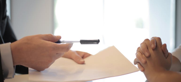 Man handing a pen and a contract to a woman.