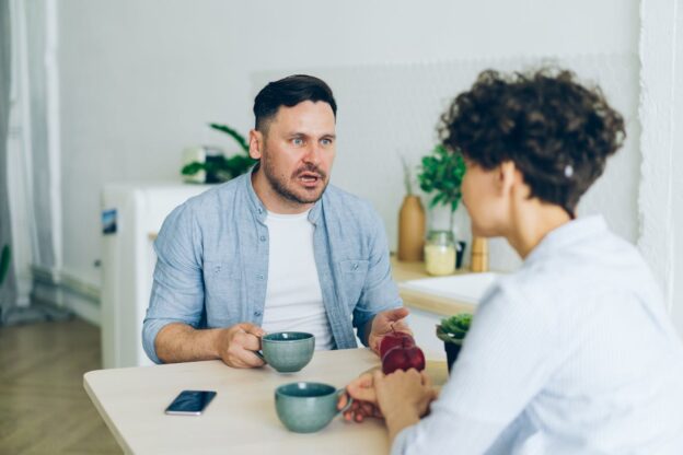 Couple fighting while sitting at a kitchen table.