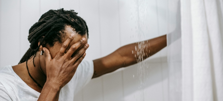 A man is holding his head in the shower and thinking about why coping with fear of failure is key to addiction recovery.