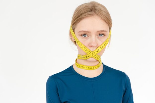 Woman with measuring tape over her mouth.