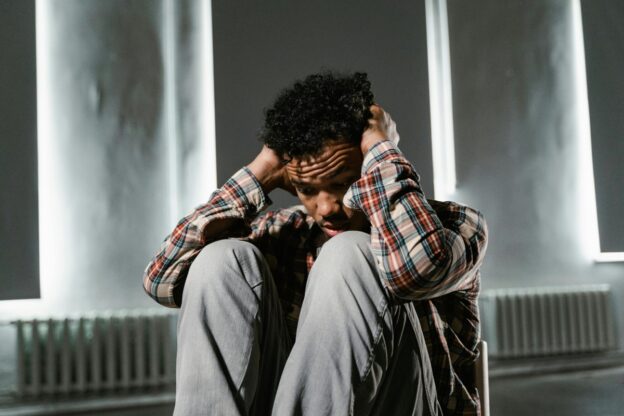 A man is sitting on the chair and holding his hands on his head.