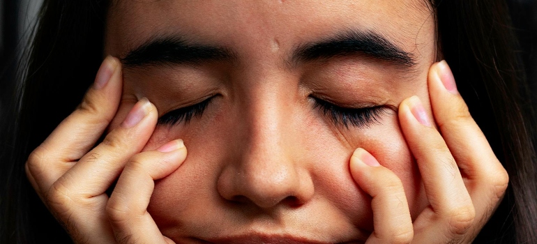 A woman is holding hands on her face with her eyes closed.
