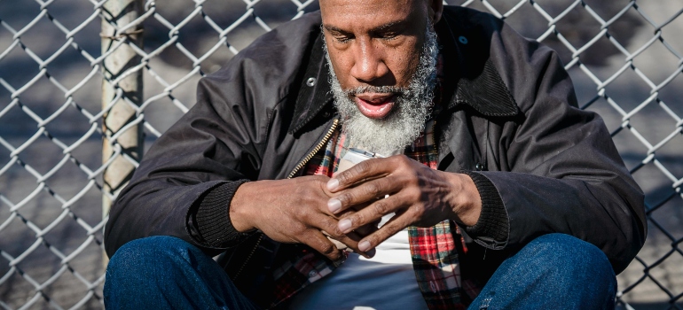 A depressed man is sitting on the street and holding a bottle of alcohol in his hand, dealing with bipolar disorder and alcohol addiction.