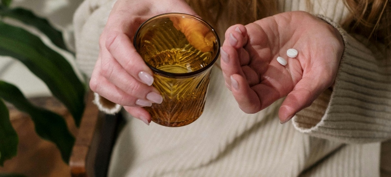 A woman is holding pills and a glass of water in her hands.