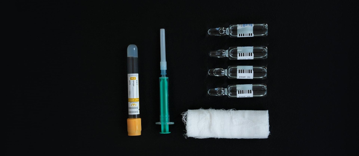 A needle, glass bottles, and medical gauze on a black surface.